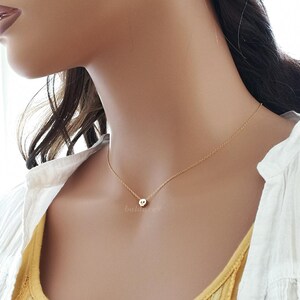 Puede incluir: Delicado collar dorado con un peque&ntilde;o colgante. El colgante tiene un dise&ntilde;o de calavera. El collar se lleva en el cuello de una persona, sobre una camiseta amarilla y una camisa blanca.