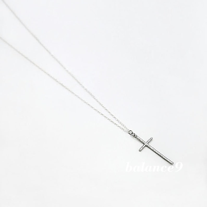 May include: A silver chain necklace with a simple silver cross pendant.