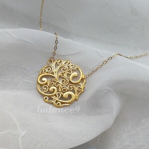 Pode incluir: Um colar de ouro com um delicado pingente circular com um design de filigrana. O pingente &eacute; feito de intrincados redemoinhos e curvas, criando um visual bonito e elegante.