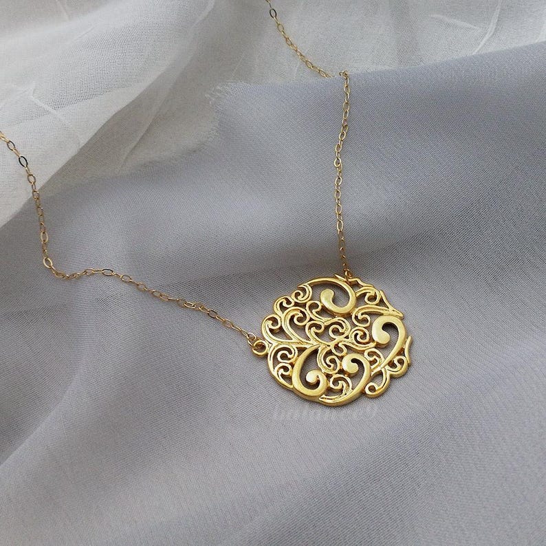 Pode incluir: Um colar de ouro com um delicado pingente circular com um design de filigrana de linhas em espiral.