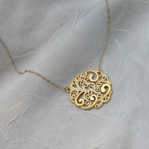 Pode incluir: Um colar de ouro com um delicado e intrincado pingente com um design circular com padr&otilde;es em espiral.