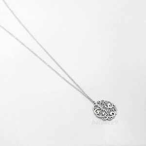 May include: A silver necklace with a delicate, circular pendant featuring a filigree design. The pendant is intricate and detailed, with a delicate, openwork pattern.