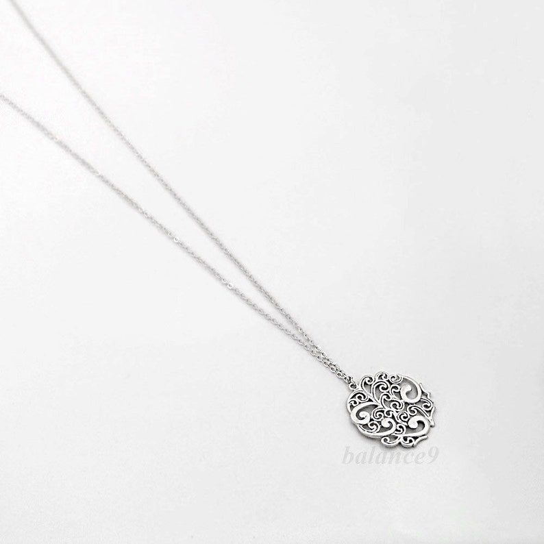 May include: A silver necklace with a delicate, circular pendant featuring a filigree design. The pendant is intricate and detailed, with a delicate, openwork pattern.