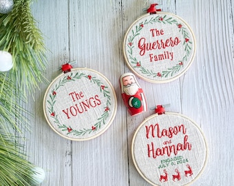 Könnte beinhalten: Drei bestickte Weihnachtsornamente mit einem grünen Kranzdesign. Die Ornamente lauten "The Youngs", "The Guerrero Family" und "Mason and Hannah Engaged July 6, 2024".