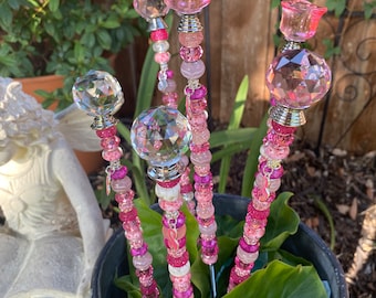 May include: Five pink and clear glass garden stakes with pink and white beads. The stakes are topped with crystal-like spheres and pink flower shapes.