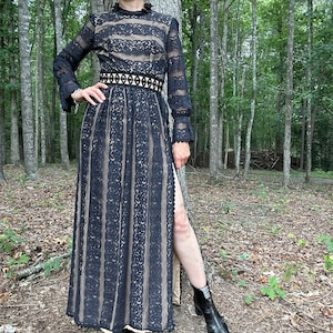 May include: A black lace maxi dress with a high neck, long sleeves, and a fitted waist. The dress has a slit up the side and is paired with black ankle boots.