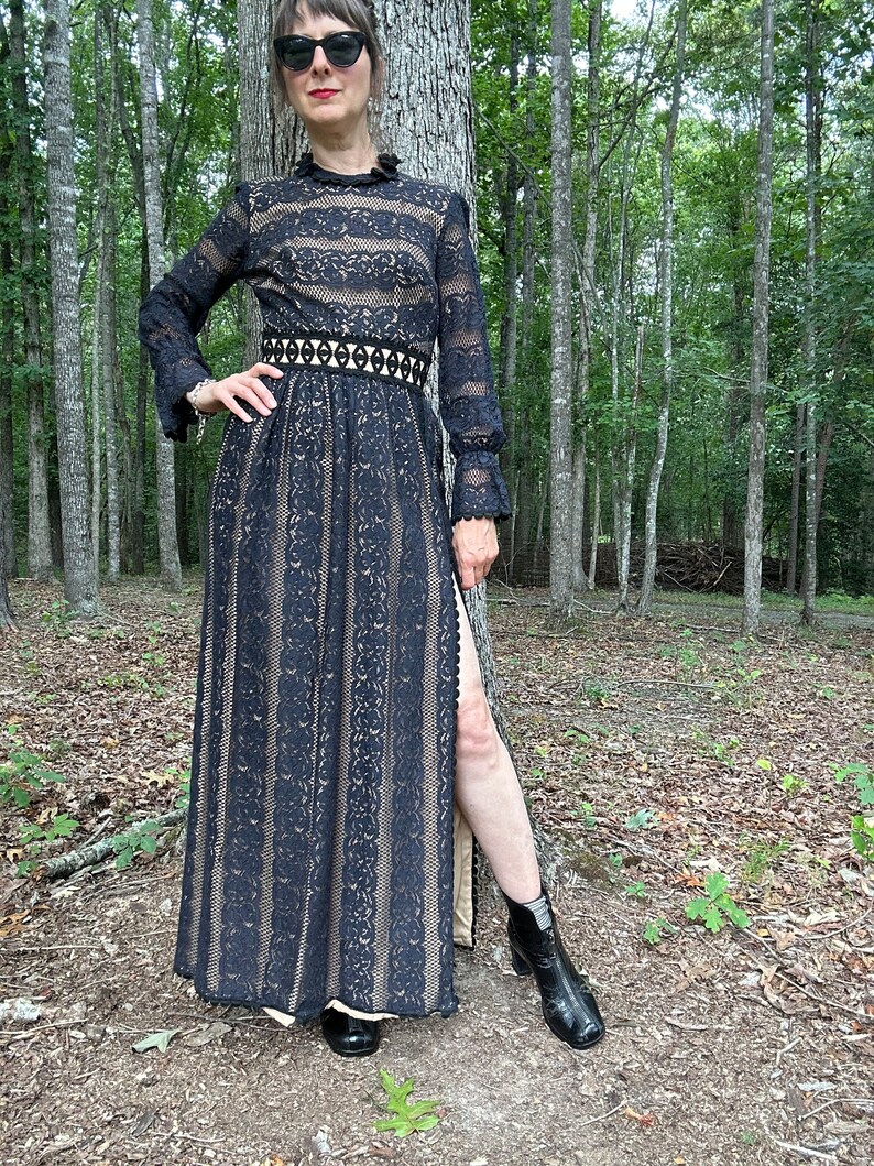 May include: A black lace maxi dress with a high neck, long sleeves, and a fitted waist. The dress has a slit up the side and is paired with black ankle boots.