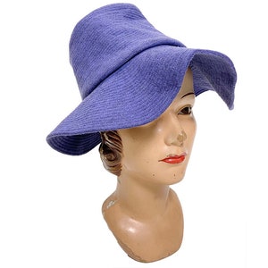 May include: A wide-brimmed hat made of a soft, textured fabric in a light purple shade. The hat has a slightly curved brim and a simple, elegant design.