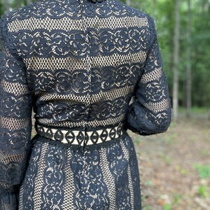 May include: Black lace dress with long sleeves and a high neck. The dress has a fitted bodice and a flowing skirt. The lace is delicate and intricate.