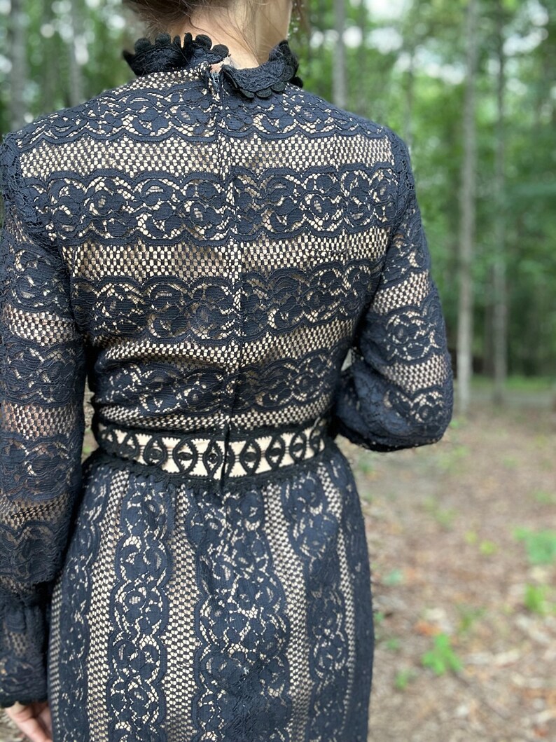 May include: Black lace dress with long sleeves and a high neck. The dress has a fitted bodice and a flowing skirt. The lace is delicate and intricate.