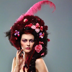 May include: A woman with dark hair styled with pink feathers and flowers, wearing a burgundy corset.