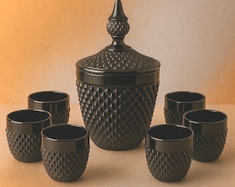 May include: A black glass candy dish with a diamond pattern and a matching lid, accompanied by six small, matching glasses. The set is displayed on a neutral surface, creating a sophisticated and elegant aesthetic.