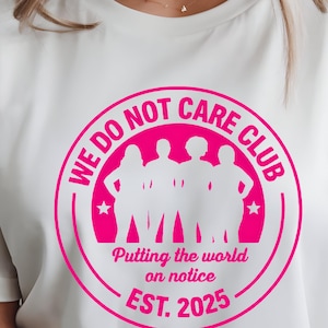 Puede incluir: Camiseta color crema con un gr&aacute;fico circular rosa. El gr&aacute;fico dice "WE DO NOT CARE CLUB" en el borde, con una silueta de cuatro figuras en el centro. Debajo de las figuras, dice "Putting the world on notice EST. 2025".