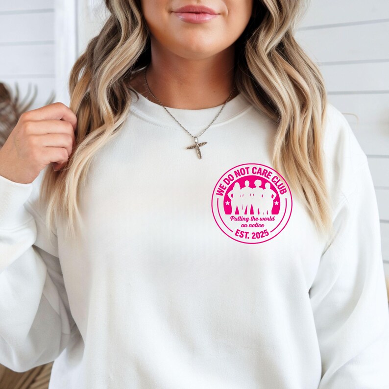 Puede incluir: Sudadera blanca con un gr&aacute;fico circular rosa que dice "WE DO NOT CARE CLUB" con una silueta de personas y el texto "Putting the world on notice. EST. 2025."