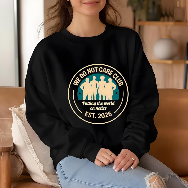 Puede incluir: Sudadera negra de cuello redondo con un gr&aacute;fico circular. El gr&aacute;fico presenta el texto "WE DO NOT CARE CLUB" alrededor de un dise&ntilde;o turquesa y beige con las palabras "Putting the world on notice EST. 2025".