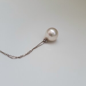 Puede incluir: Un collar con un colgante de perla blanca en una cadena de plata delicada.
