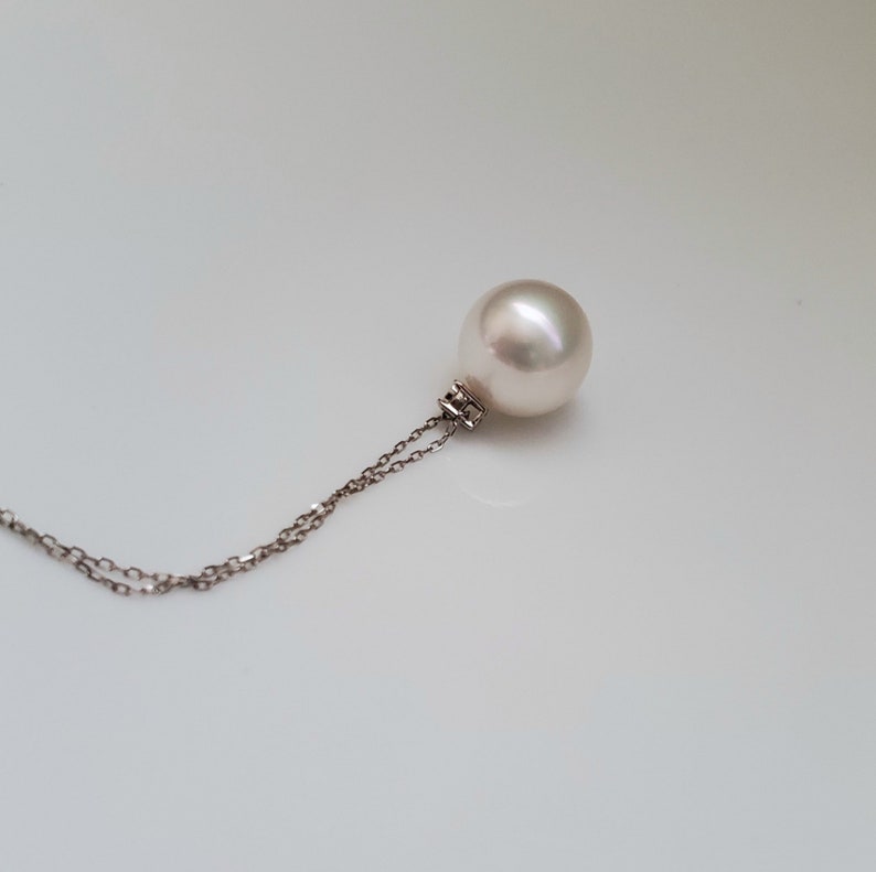 Puede incluir: Un collar con un colgante de perla blanca en una cadena de plata delicada.