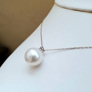 Puede incluir: Un collar con un colgante de perla blanca y una cadena de plata. La perla es grande y redonda.