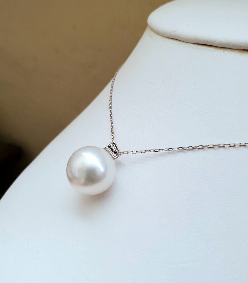 Puede incluir: Un collar con un colgante de perla blanca y una cadena de plata. La perla es grande y redonda.
