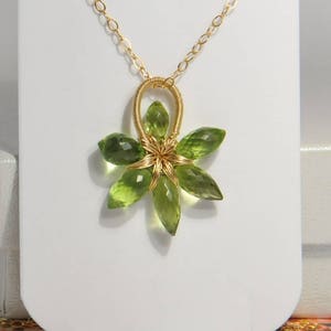 Könnte beinhalten: Eine goldene Kettenkette mit einem Anhänger aus grünem Edelstein in Form einer Blume. Die Blume besteht aus Draht, der um die Edelsteine gewickelt ist.