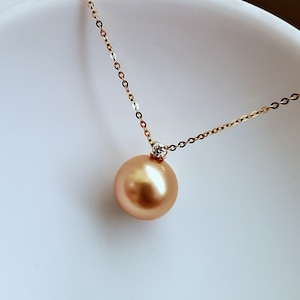 K&ouml;nnte beinhalten: Eine goldene Kettenkette mit einem gro&szlig;en goldenen Perlenanh&auml;nger und einem kleinen Diamantenakzent.