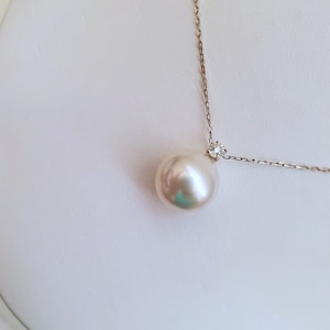 Puede incluir: Un collar con un colgante de perla blanca y un peque&ntilde;o acento de diamante. La perla es grande y redonda, y la cadena es delicada.