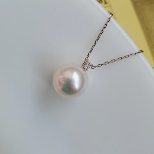 Puede incluir: Un collar con un colgante de perla blanca y un peque&ntilde;o acento de diamante. La perla es grande y redonda, y la cadena es delicada.