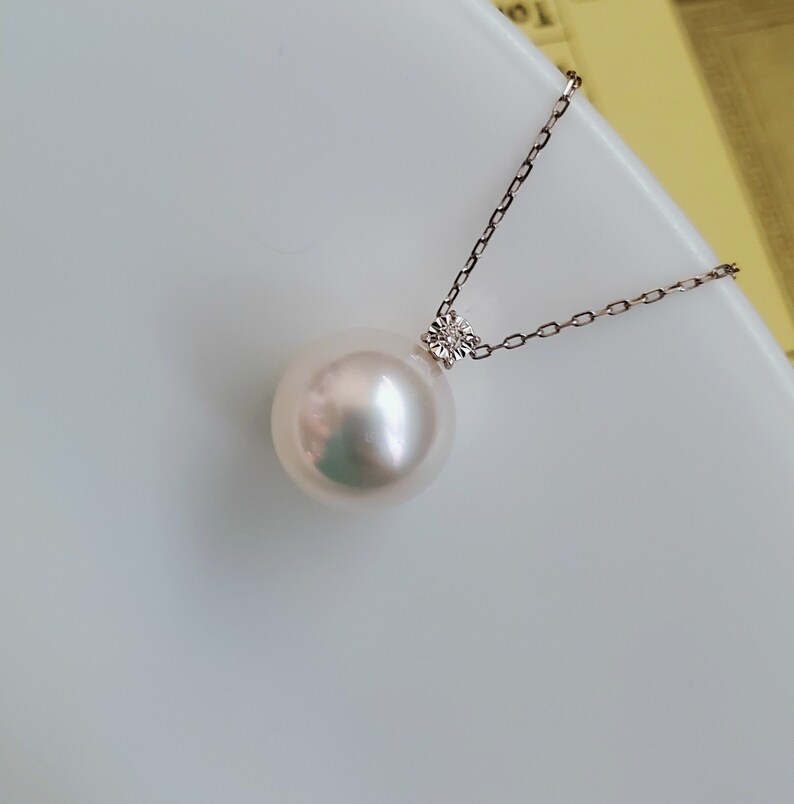 Puede incluir: Un collar con un colgante de perla blanca y un peque&ntilde;o acento de diamante. La perla es grande y redonda, y la cadena es delicada.