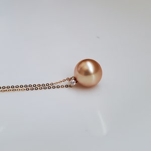 K&ouml;nnte beinhalten: Eine goldene Kettenkette mit einem gro&szlig;en, runden, goldenen Perlenanh&auml;nger und einem kleinen Diamanten-Akzent.