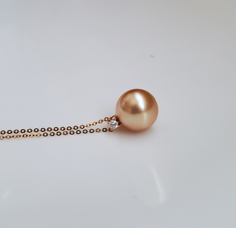 K&ouml;nnte beinhalten: Eine goldene Kettenkette mit einem gro&szlig;en, runden, goldenen Perlenanh&auml;nger und einem kleinen Diamanten-Akzent.