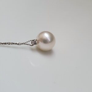 Puede incluir: Un collar con un colgante de perla blanca y un peque&ntilde;o acento de diamante. La perla es redonda y lisa, y la cadena es delicada.
