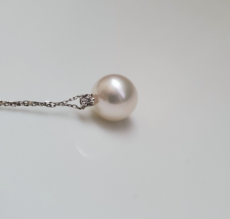 Puede incluir: Un collar con un colgante de perla blanca y un peque&ntilde;o acento de diamante. La perla es redonda y lisa, y la cadena es delicada.