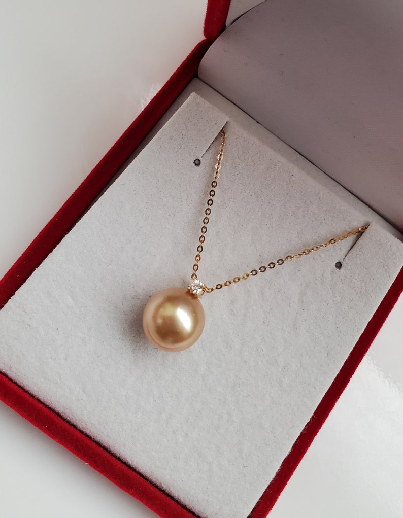 K&ouml;nnte beinhalten: Eine goldene Kettenkette mit einem gro&szlig;en goldenen Perlenanh&auml;nger. Die Perle befindet sich in einer roten Samt-Schmuckschatulle.