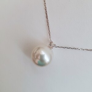 Puede incluir: Un collar con un colgante de perla blanca y un peque&ntilde;o acento de diamante en una cadena de plata.
