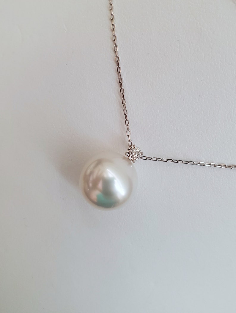 Puede incluir: Un collar con un colgante de perla blanca y un peque&ntilde;o acento de diamante en una cadena de plata.