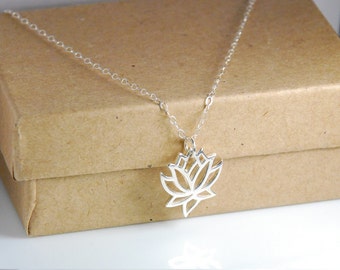 Puede incluir: Un collar de cadena de plata con un delicado colgante de flor de loto calado. El collar se muestra en una caja de papel marrón.