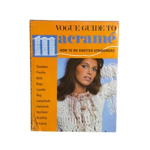 May include: A vintage book titled Vogue Guide to Macramé: How to Do Knotted Stringwork. The orange cover features a photograph of a person wearing a white crocheted top with fringe and a knotted necklace, alongside a list of projects including sweaters, ponchos, belts, bags, layette, rugs, lampshades, hammocks, necklaces, braiding, and fringing.