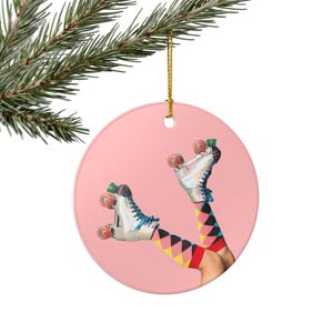 May include: A round, pink Christmas ornament featuring a whimsical design of roller skates and legs with colorful socks. The skates are white with blue laces and red wheels. The socks have a diamond pattern.