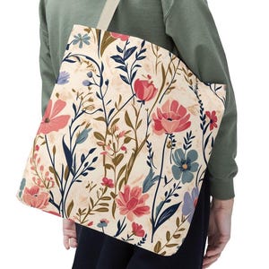 Könnte beinhalten: Tragetasche mit floralem Muster. Die Tasche hat einen cremefarbenen Hintergrund mit einem sich wiederholenden Design aus rosa, blauen und marinefarbenen Blumen und grünen Stielen. Die Tragetasche hat einen cremefarbenen Riemen.