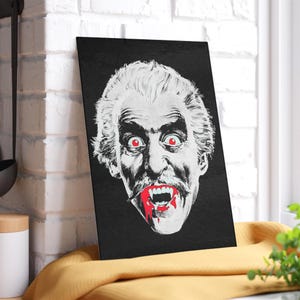 Puede incluir: Arte mural rectangular negro que presenta un retrato estilizado en blanco y negro de un vampiro con ojos rojos y sangre goteando de sus colmillos. La obra de arte tiene una estética de película de terror vintage.