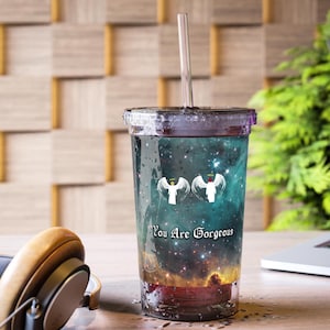 May include: A clear tumbler with a lid and straw, featuring a celestial design with two angel figures and the text "You Are Gorgeous." The cup has a galaxy-themed background with shades of blue, red, and yellow.