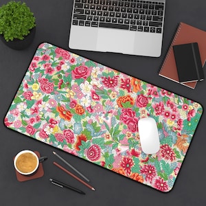 Puede incluir: Una alfombrilla de ratón rectangular con estampado floral y borde negro. El diseño presenta un denso patrón de flores rosas, rojas, naranjas, amarillas y azules sobre un fondo verde claro y blanco. Un ratón de ordenador blanco está encima.