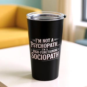 May include: Black travel tumbler with a clear lid. The tumbler features the text "I'M NOT A PSYCHOPATH... I'M A HIGH-FUNCTIONING SOCIOPATH" in white and pink lettering. The tumbler is cylindrical and appears to be made of stainless steel.