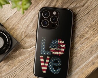 Può includere: Custodia per telefono nera con la scritta "LOVE" nei colori patriottici. La "L" e la "E" sono blu con stelle bianche, la "O" è un girasole con strisce rosse e bianche e la "V" è a strisce rosse e bianche.