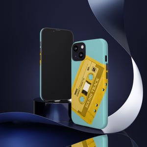 May include: Two phone cases, one black and one light blue. The light blue case features a yellow cassette tape design with the words "SOUND TRACK" and "INDEX COMPACT CASSETTE". The black phone case is plain.