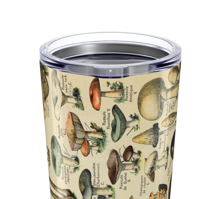 May include: A stainless steel travel mug featuring a vintage botanical illustration of various mushrooms. The design includes detailed drawings of different species with French labels, set against a cream-colored background.