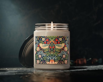 May include: A lit candle in a glass jar with a decorative label. The label features a detailed pattern of birds, strawberries, and flowers in shades of blue, green, red, and yellow. The jar's lid is open, and the candle is on a dark surface.