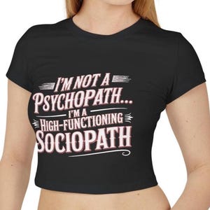 May include: Black crop top with the text "I'M NOT A PSYCHOPATH... I'M A HIGH-FUNCTIONING SOCIOPATH" in white and pink lettering. The shirt has short sleeves and a crew neck.