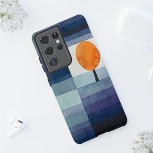 May include: A smartphone case featuring a watercolor design. The case has a blue and purple striped background with an orange tree illustration. The phone case is black and has a camera module.