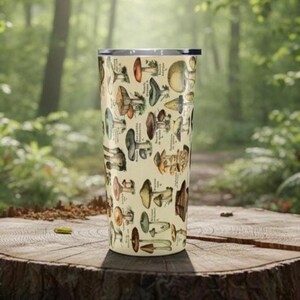 May include: A beige travel mug featuring a detailed illustration of various mushrooms in shades of brown, green, and yellow. The design includes scientific labels. The mug is cylindrical and has a silver rim and lid.